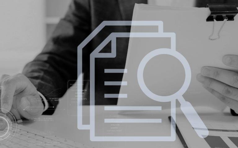 grayscale image of man&#039;s hand typing on computer while holding paper