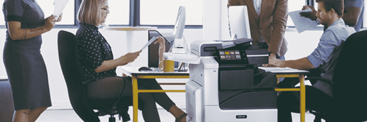 Five people around a desk with the Xerox VersaLink C7130 in front of it