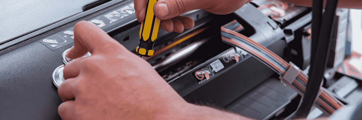 A person fixing a printer with a yellow and black screwdriver while holding a stethoscope on the machine
